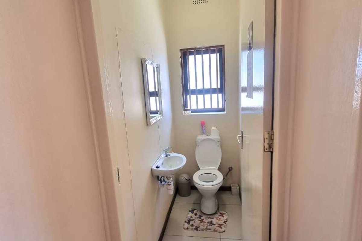 A compact office restroom featuring a wall-mounted basin, a standard toilet, and tiled flooring with a small window for ventilation.