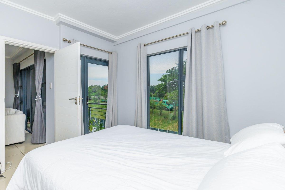 A bright bedroom featuring modern grey-toned walls, crown molding, and a glass door providing access to a private balcony with scenic views.