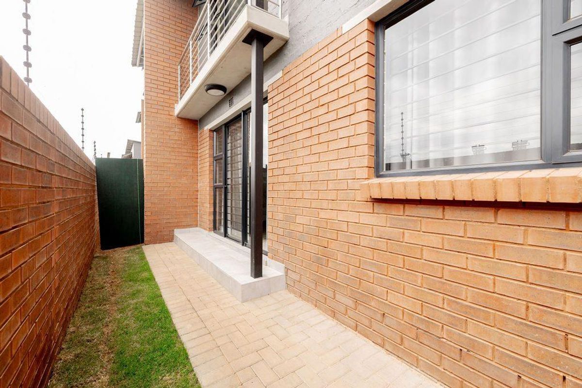 A private rear courtyard featuring brick paving, a small grass strip, and direct access to the apartment via sliding glass doors.