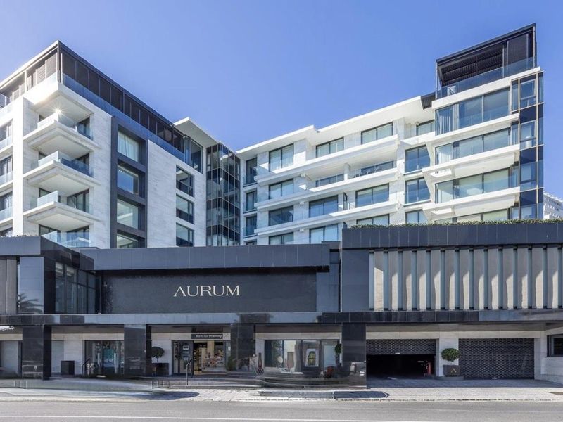 Modern multi-story apartment building facade featuring stone and black granite cladding, glass balconies, and a secure underground parking entrance.