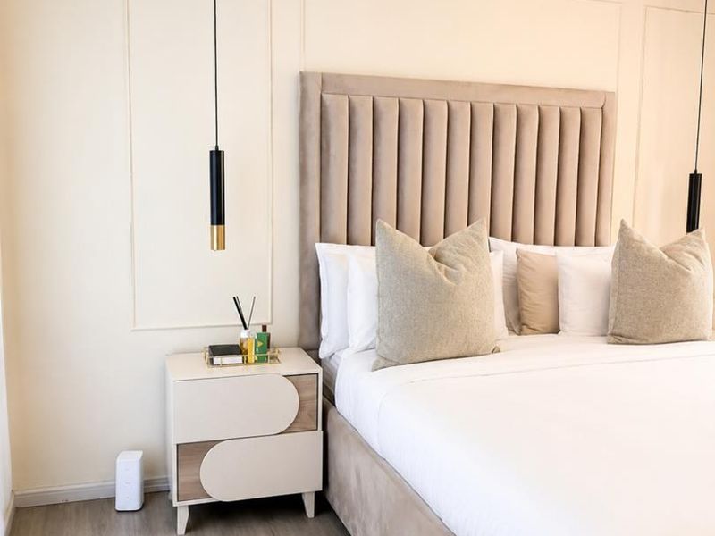A well-maintained bedroom featuring modern pendant lighting, decorative wall molding, and light-toned laminate flooring.