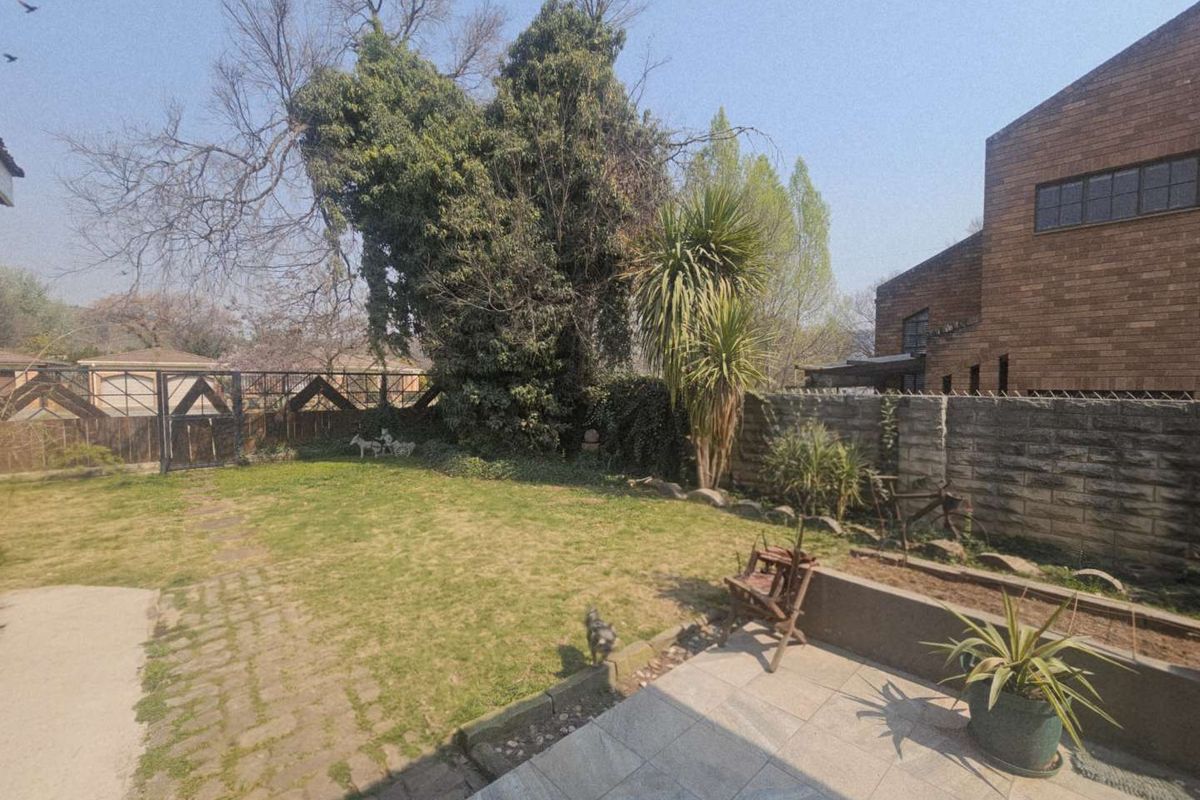 A private rear garden featuring a paved patio area, established trees, and a brick boundary wall, offering a quiet outdoor space.