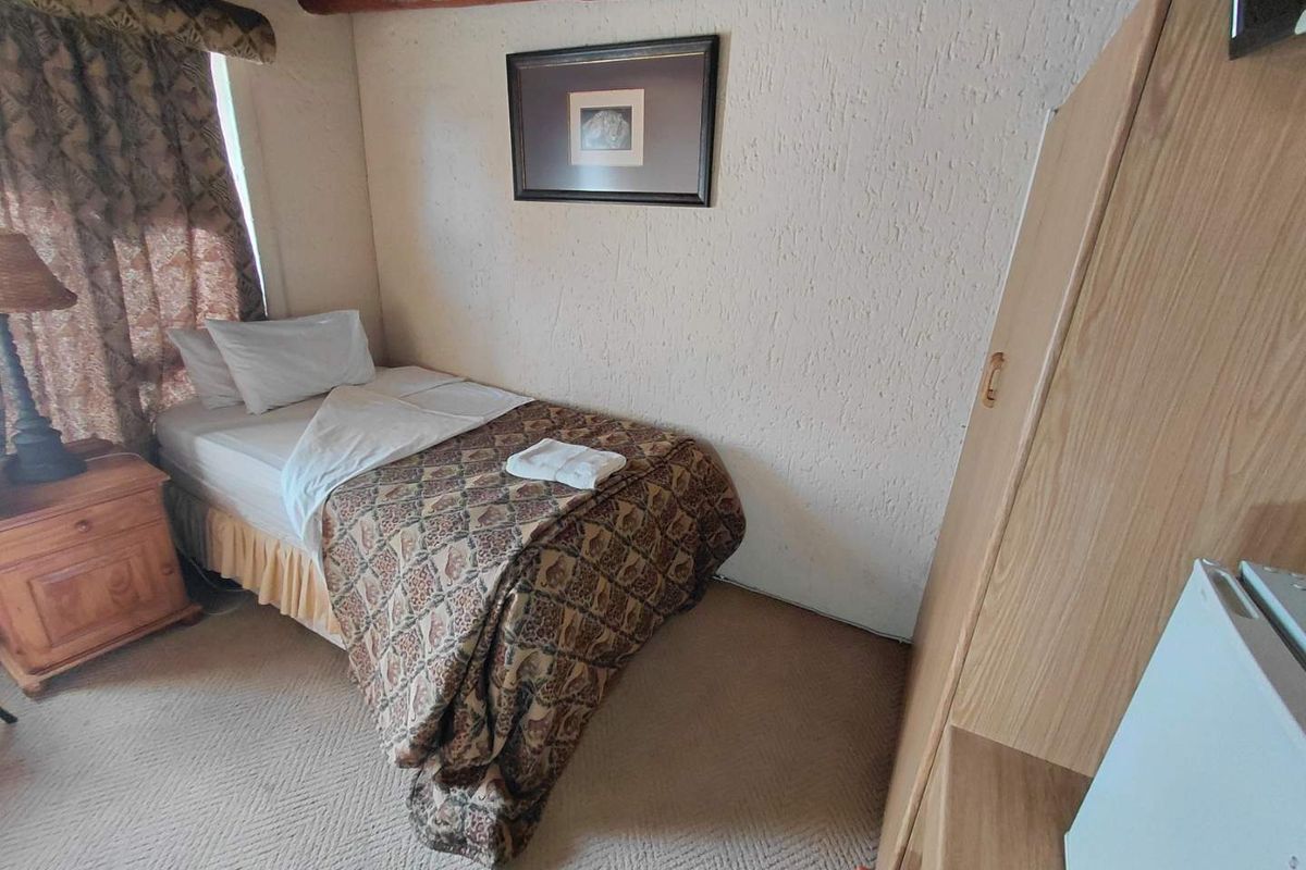 A compact bedroom featuring exposed timber ceiling beams, textured wall finishes, and fitted carpeting.