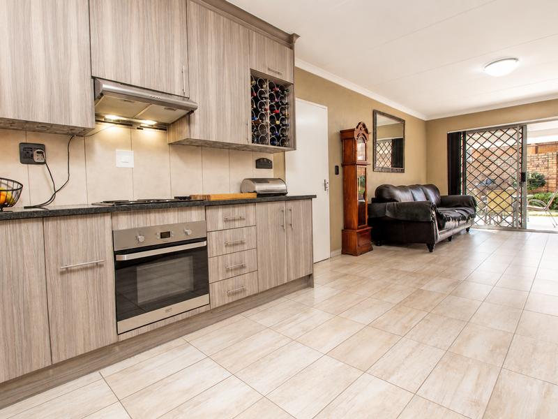 Open-plan kitchen and living area featuring modern wood-look cabinetry, built-in appliances, tiled flooring, and direct access to an outdoor patio through sliding doors.