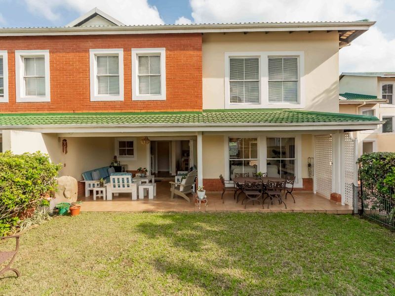 Rear view of the townhouse featuring a covered tiled patio, brick and plaster facade, and access to a private garden area.