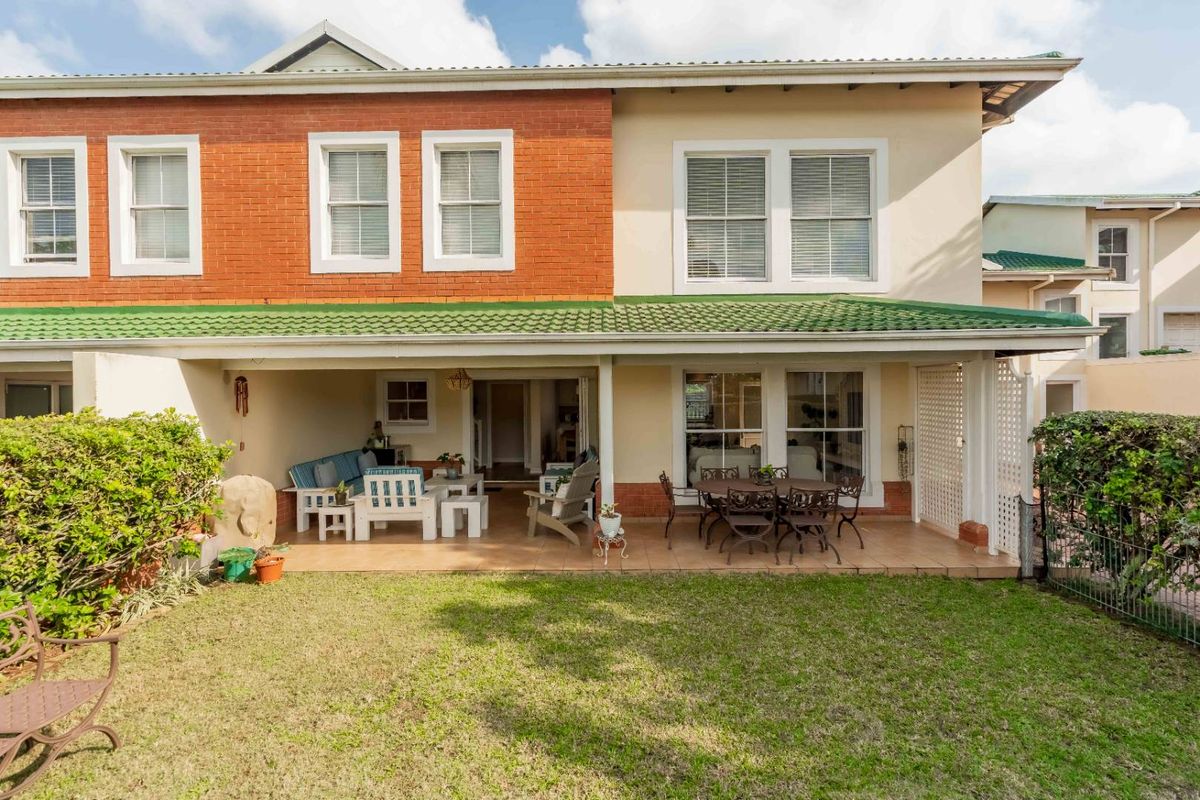 Rear view of the townhouse featuring a covered tiled patio, brick and plaster facade, and access to a private garden area.