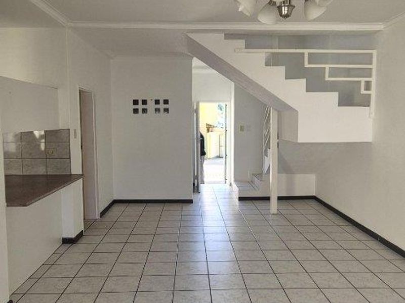 An open-plan living area featuring tiled flooring, a staircase, and a kitchen counter, offering a blank canvas for interior design.