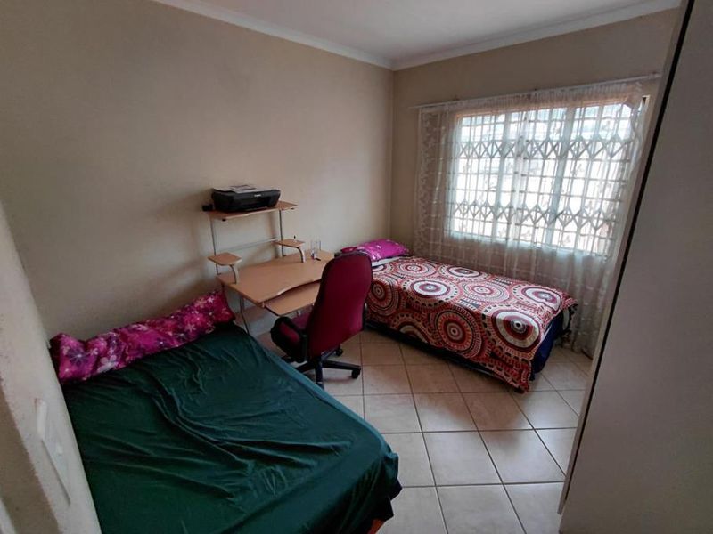 A functional bedroom featuring tiled flooring, a window with a security gate, and built-in cupboard storage.