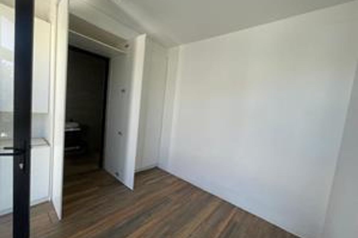 A bright, empty bedroom featuring modern timber flooring and a built-in wardrobe with clean white finishes.