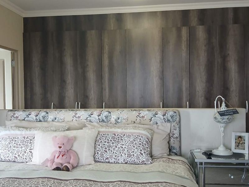 A well-maintained bedroom featuring extensive floor-to-ceiling built-in cupboards with a dark wood finish and decorative coving.