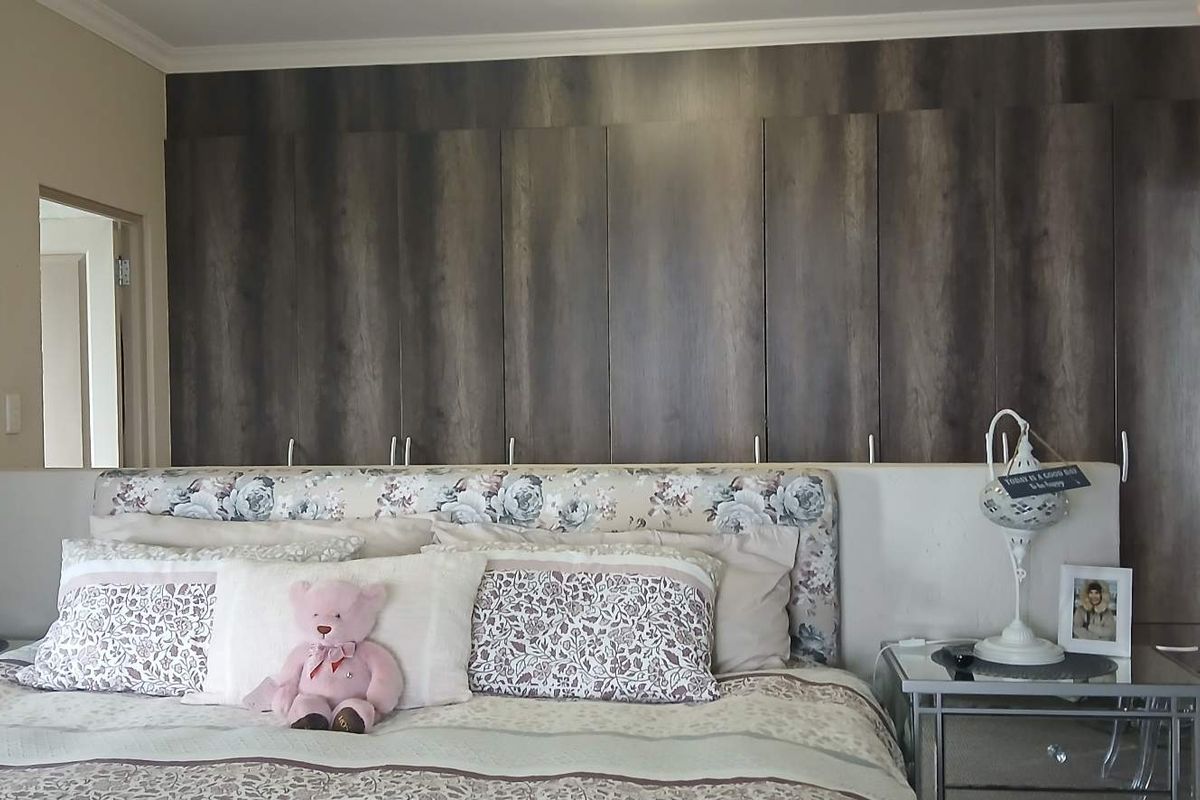 A well-maintained bedroom featuring extensive floor-to-ceiling built-in cupboards with a dark wood finish and decorative coving.