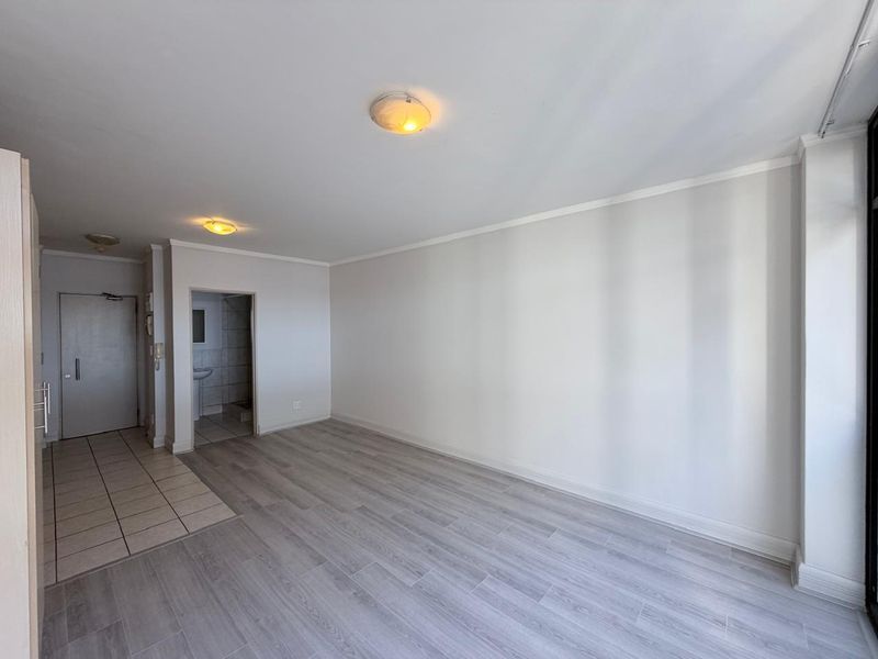 A bright, empty living area featuring a combination of tiled and laminate flooring, neutral walls, and flush mount ceiling lighting.