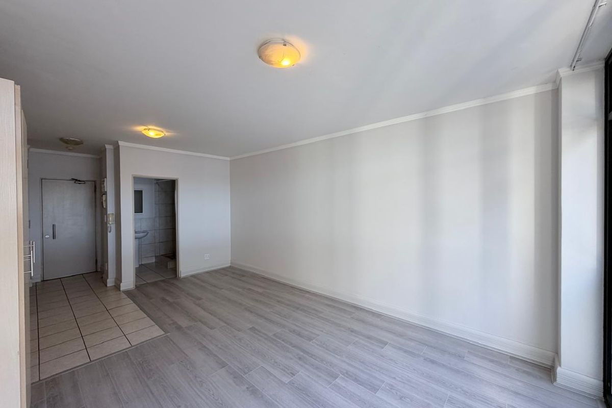A bright, empty living area featuring a combination of tiled and laminate flooring, neutral walls, and flush mount ceiling lighting.