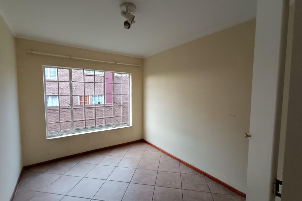 A vacant bedroom featuring tiled flooring, a large window with security bars, and a central ceiling light fixture.