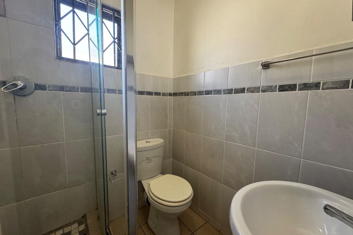 A functional bathroom featuring a glass-enclosed shower, pedestal basin, and neutral ceramic tiling throughout.