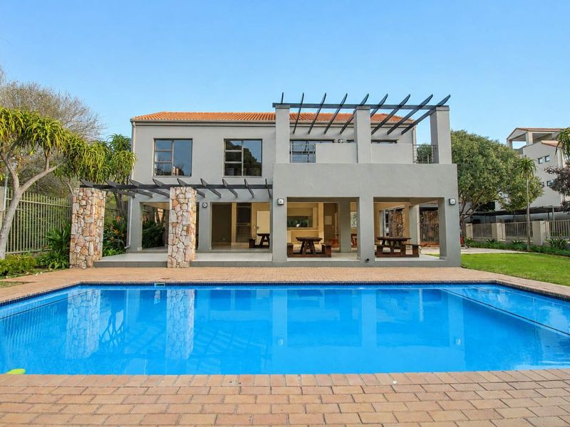 Rear view of the property featuring a swimming pool, brick-paved surround, and a covered patio area with stone-clad pillars and a pergola.
