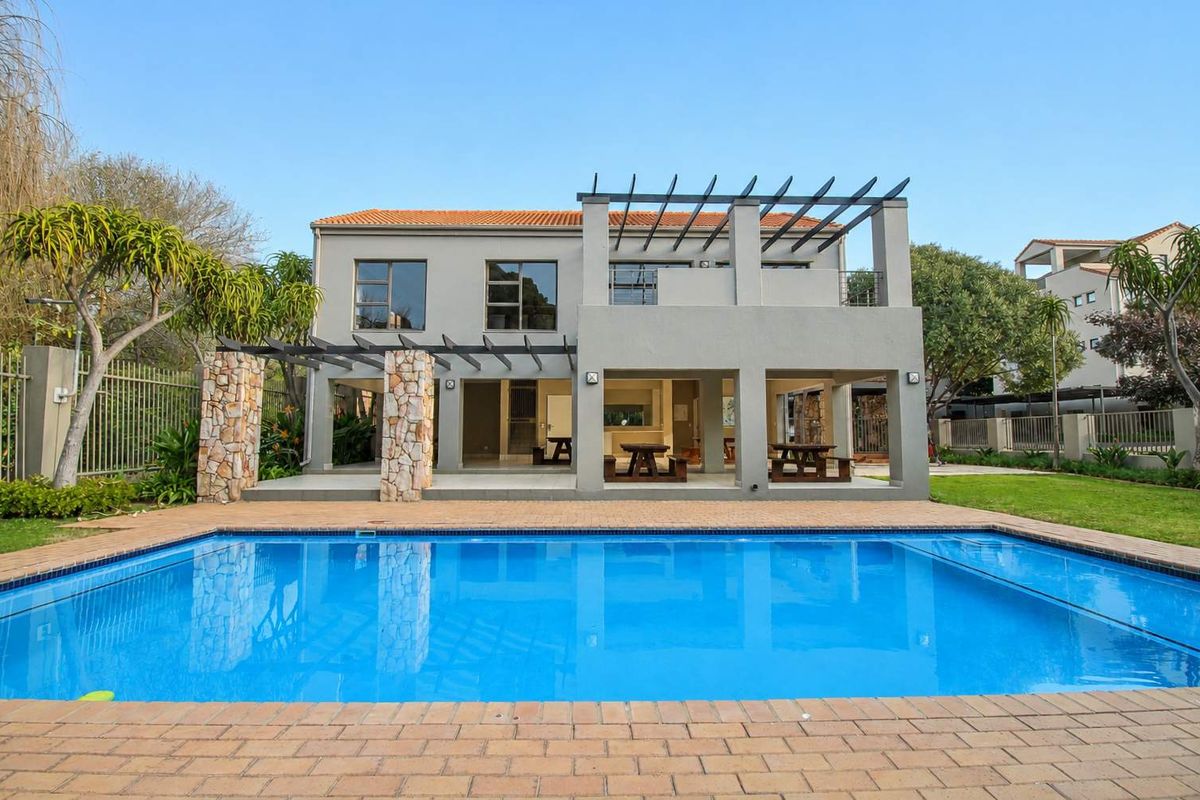 Rear view of the property featuring a swimming pool, brick-paved surround, and a covered patio area with stone-clad pillars and a pergola.