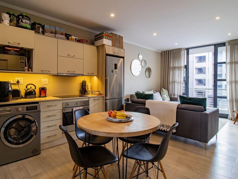 Modern open-plan apartment featuring a compact kitchen with integrated cabinetry, built-in oven and hob, and a seamless transition to the living area and balcony.