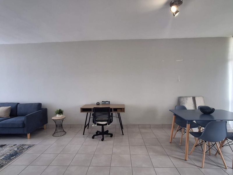 An open-plan living and dining area featuring neutral tiled flooring and track lighting, offering a versatile space for various furniture arrangements.