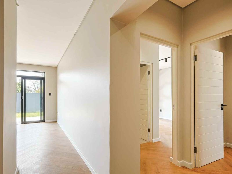 A bright, modern hallway featuring high-quality herringbone timber flooring and clean, neutral walls, leading to multiple rooms and an outdoor access point.