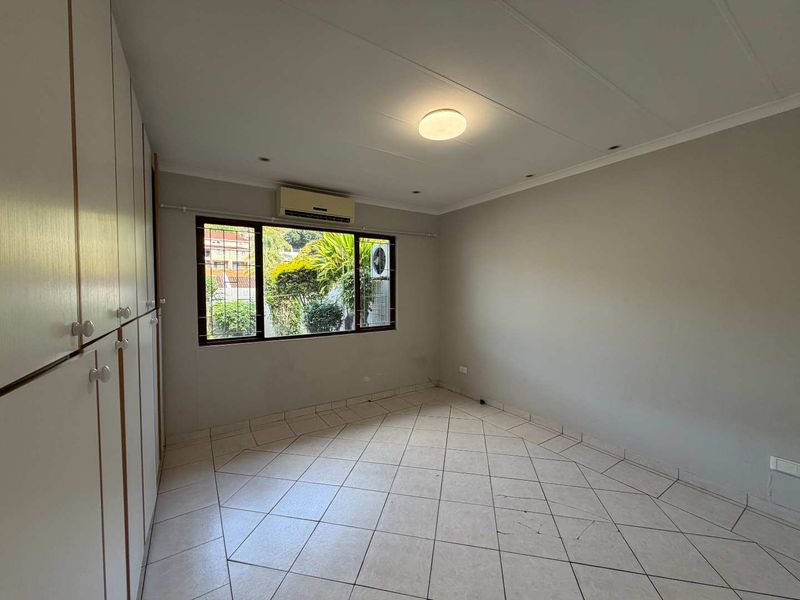 A spacious, empty bedroom featuring neutral tiled flooring, extensive built-in cupboard storage, and an integrated air conditioning unit.