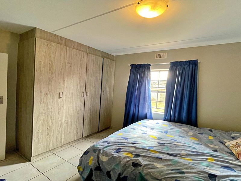 A functional bedroom featuring built-in wood-look cupboards, tiled flooring, and a window providing natural light.