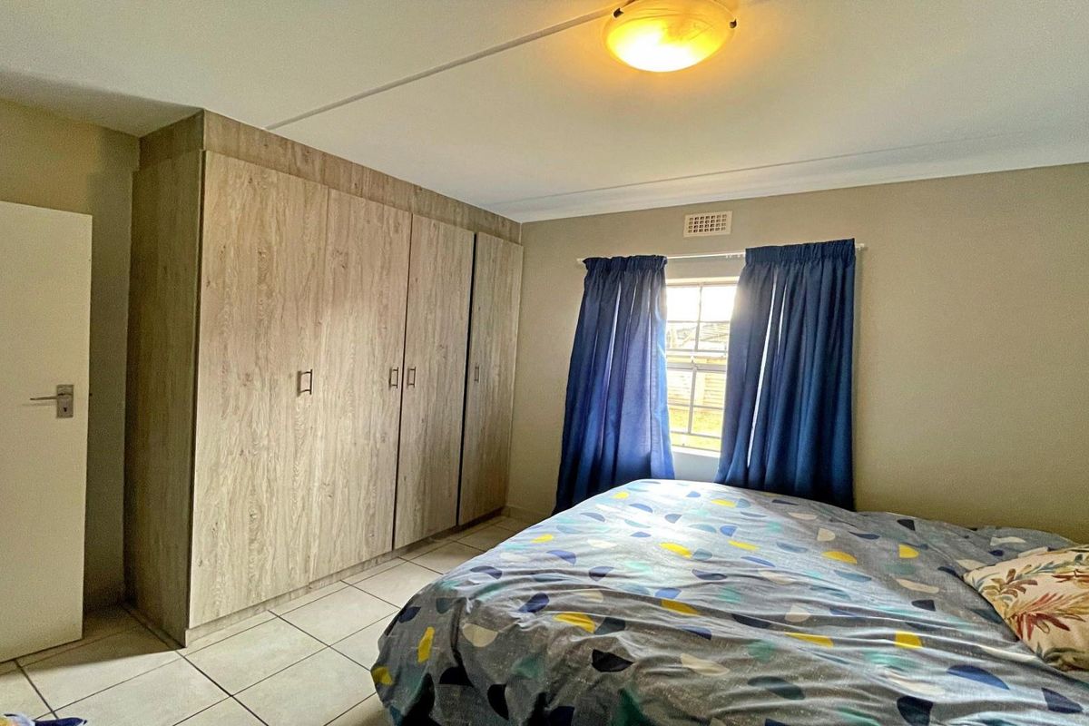 A functional bedroom featuring built-in wood-look cupboards, tiled flooring, and a window providing natural light.