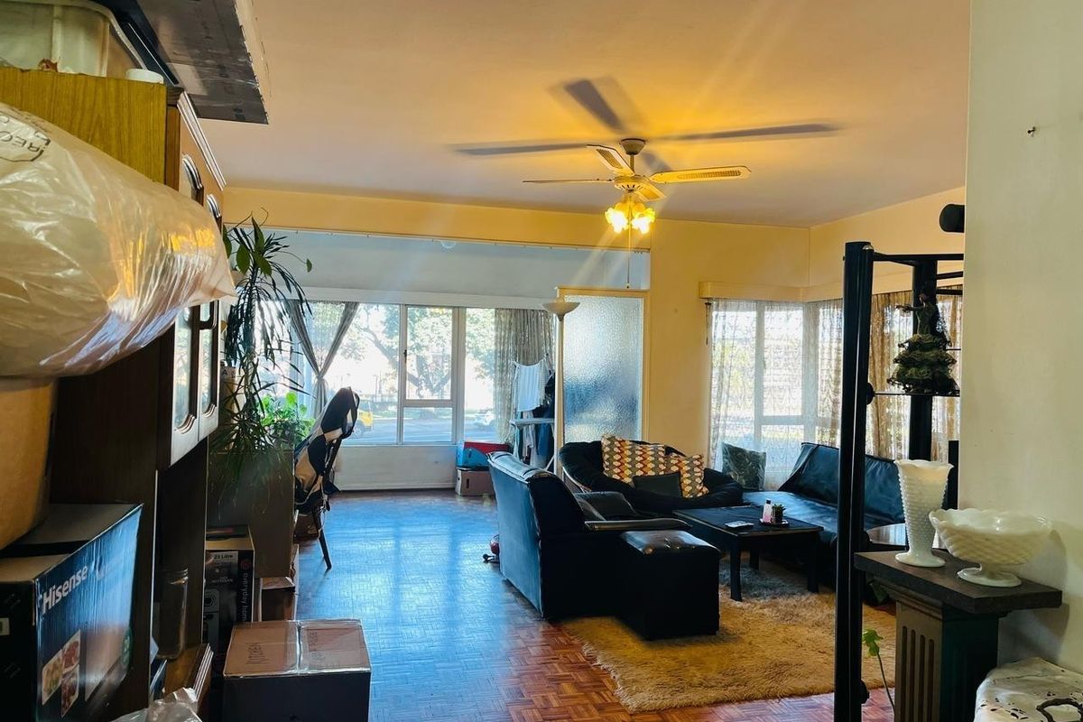 Spacious living area featuring classic parquet flooring, a ceiling fan, and large windows that provide ample natural light.