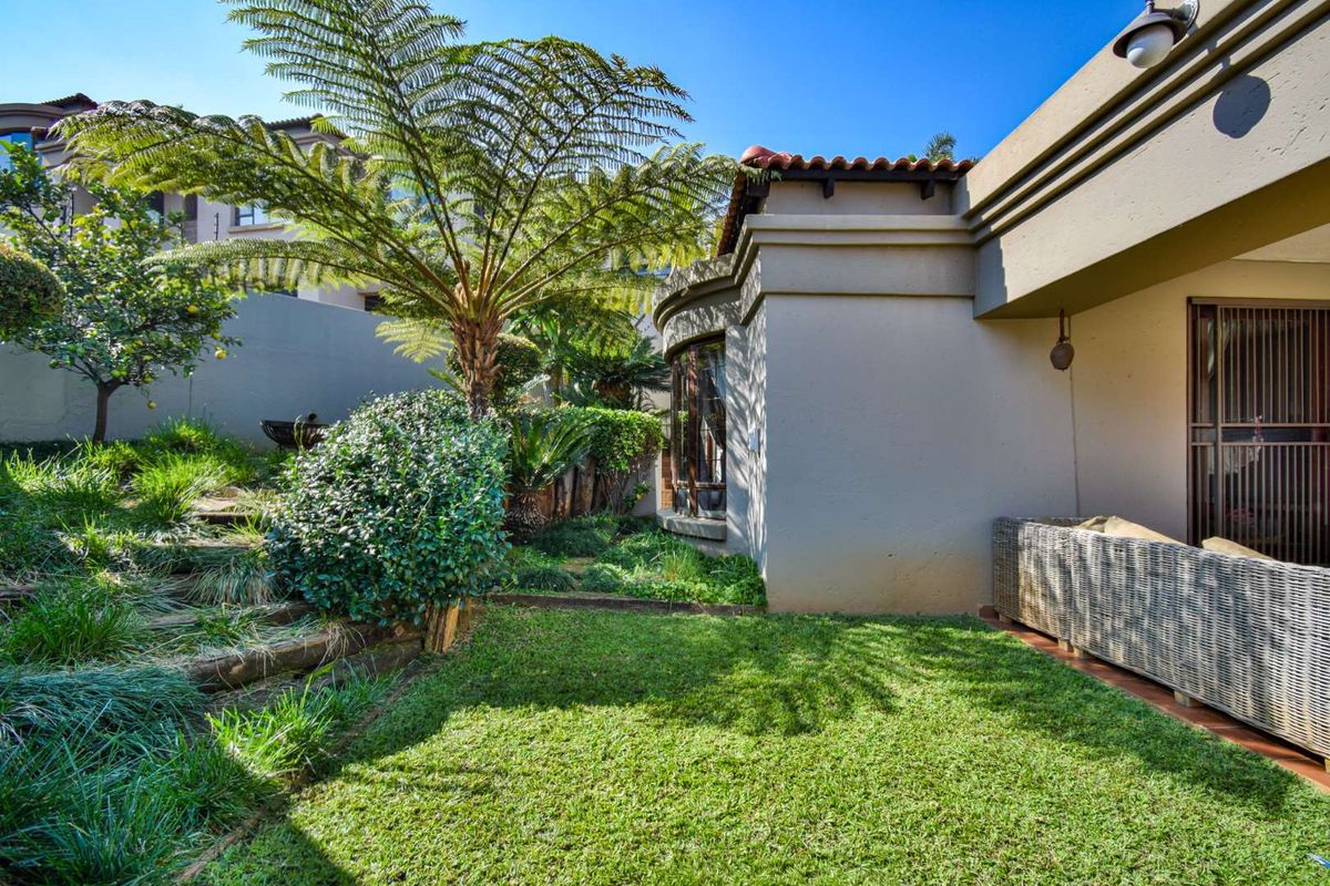 A well-maintained rear garden featuring a manicured lawn, established tree fern, and a covered patio area adjacent to the home's exterior.