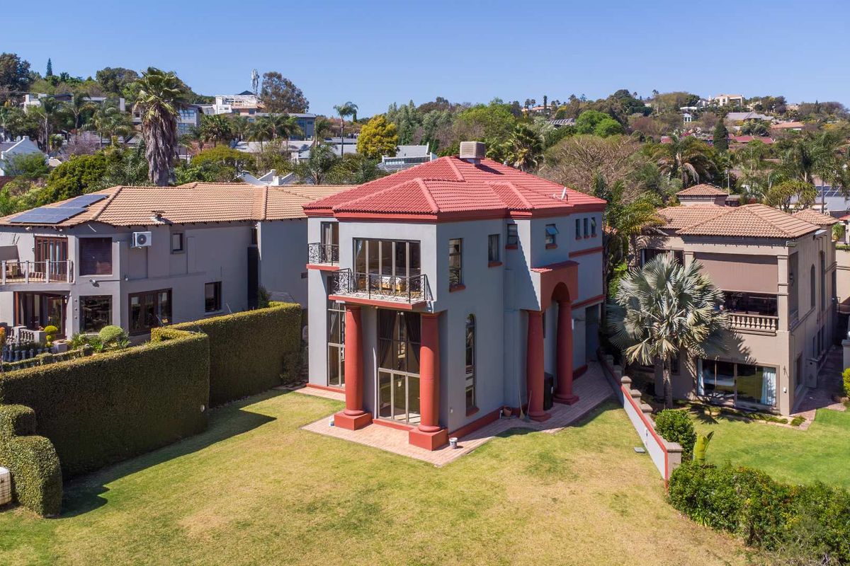 Aerial view of the rear elevation featuring a multi-story residence with a tiled roof, balcony, and a well-maintained garden with paved patio area.