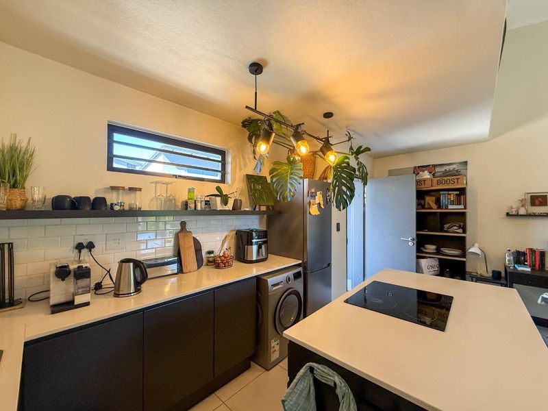 Modern kitchen featuring dark cabinetry, stone countertops, a central island with an induction cooktop, subway tile backsplash, and integrated laundry facilities.