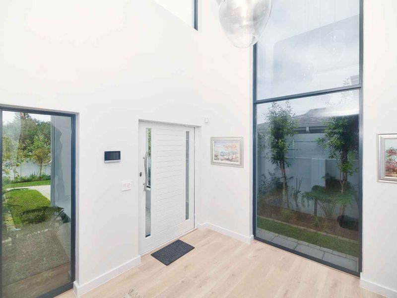 Bright and spacious double-volume entrance hall featuring modern timber flooring, full-height glass windows, and a contemporary front door.