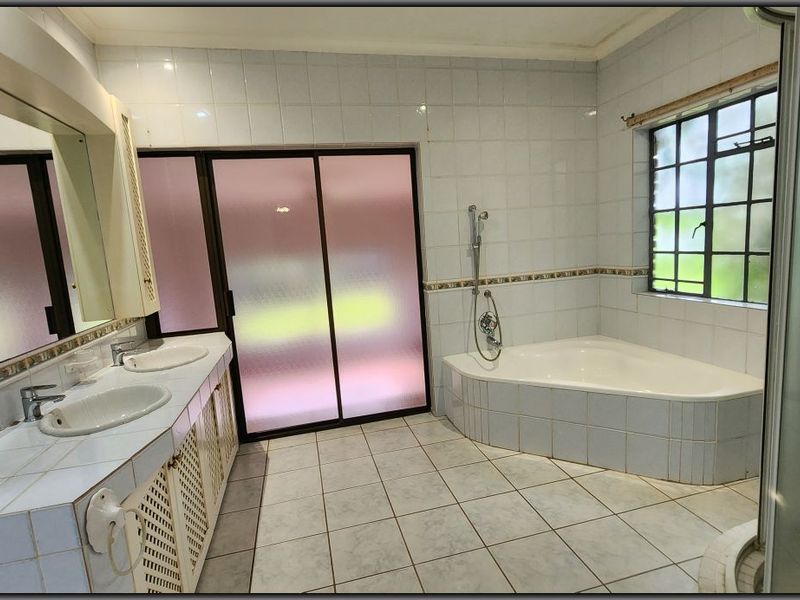 Spacious bathroom featuring a double vanity, corner bathtub, and separate shower enclosure with neutral wall and floor tiling.