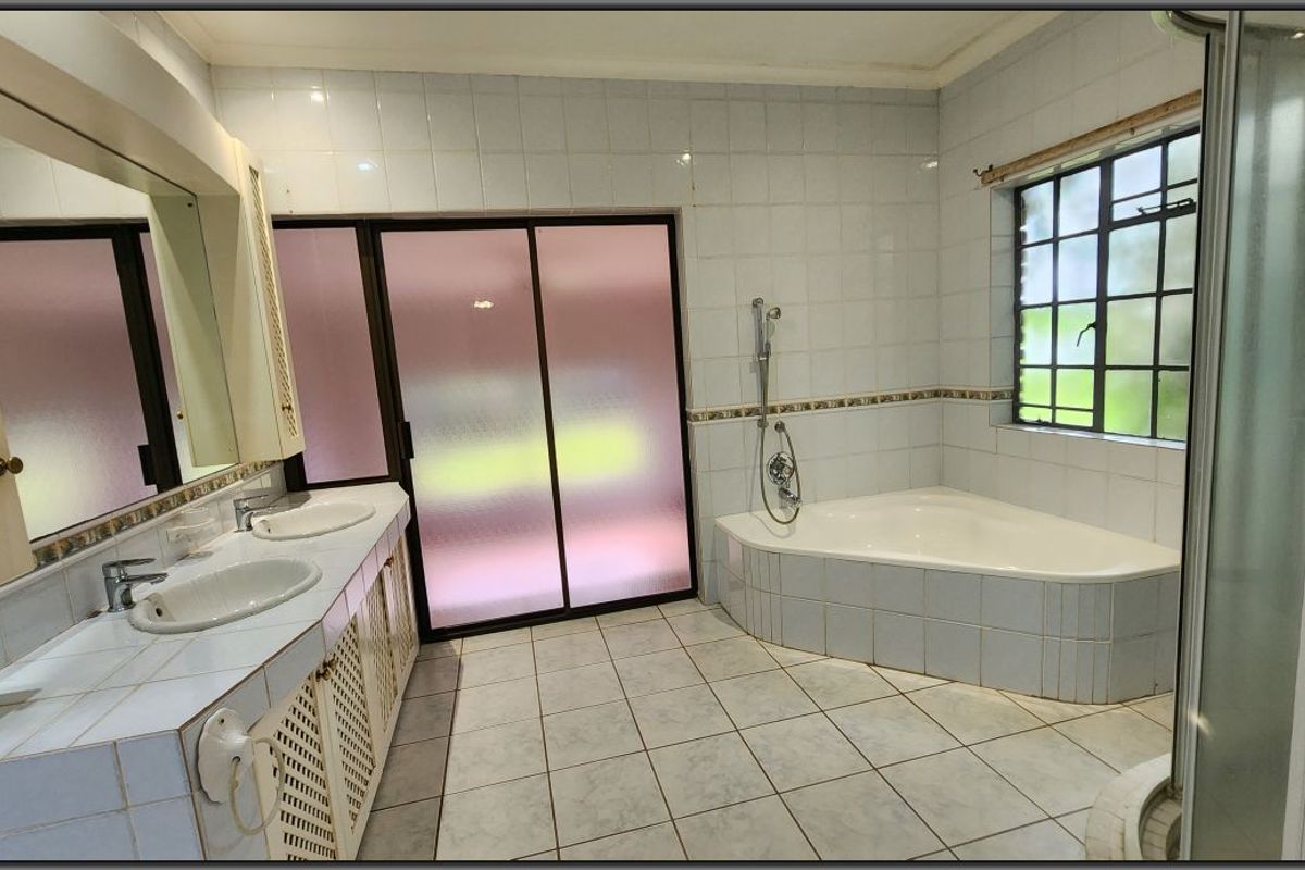 Spacious bathroom featuring a double vanity, corner bathtub, and separate shower enclosure with neutral wall and floor tiling.