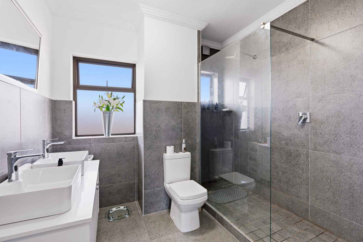 Modern bathroom featuring a double vanity, walk-in shower with glass screen, and contemporary grey wall and floor tiling.