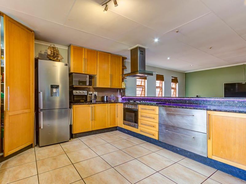 A functional kitchen featuring wooden cabinetry, granite countertops, a breakfast bar with integrated lighting, and stainless steel appliances including a built-in oven and extractor.