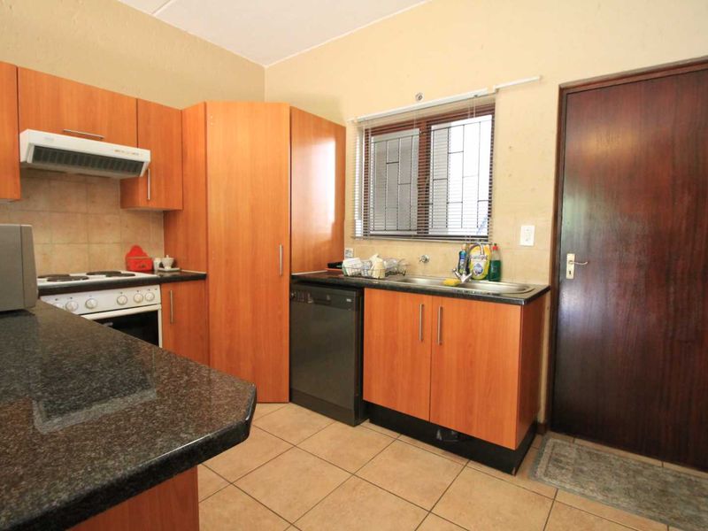 A functional kitchen featuring laminate cabinetry, granite countertops, built-in oven with hob, extractor fan, and tiled flooring with a window for natural light.