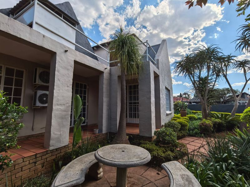 Rear view of the property featuring a covered patio with terracotta tiles, established garden, and upper-level balcony access.