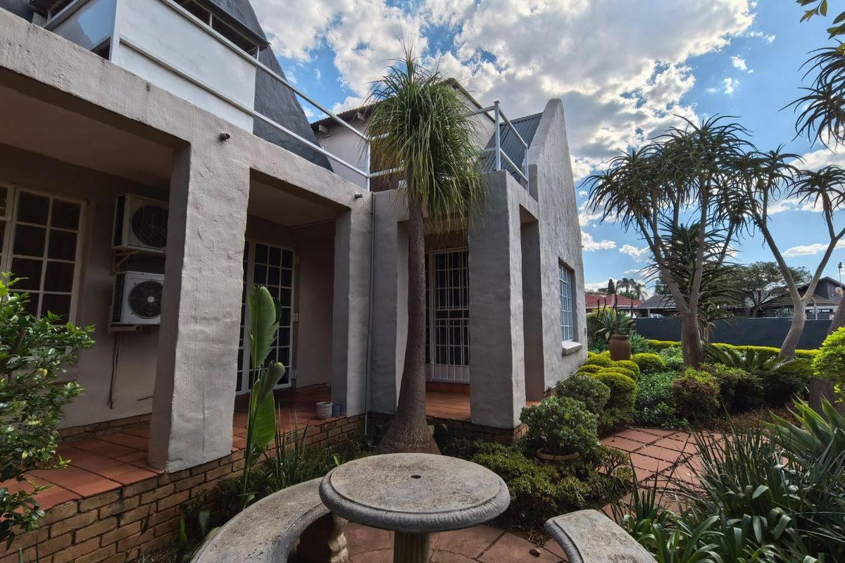 Rear view of the property featuring a covered patio with terracotta tiles, established garden, and upper-level balcony access.