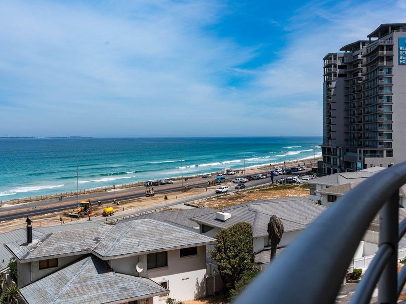Elevated coastal view overlooking the beach, ocean, and surrounding residential area from a balcony.