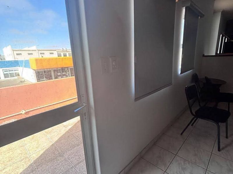 Interior view of a balcony area featuring tiled flooring, roller blinds, and a glass door leading to an outdoor space.