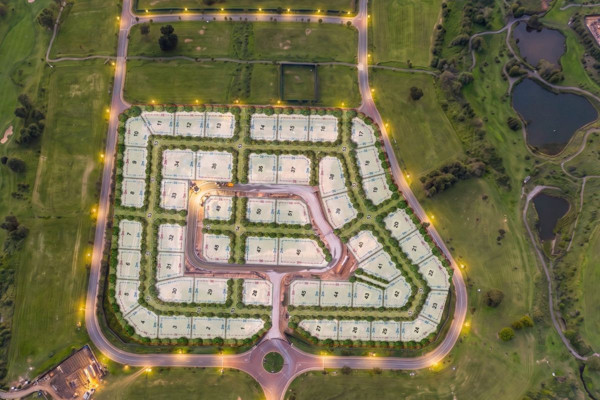 An aerial view of a residential estate development featuring subdivided plots, paved internal roads, street lighting, and surrounding golf course landscape.