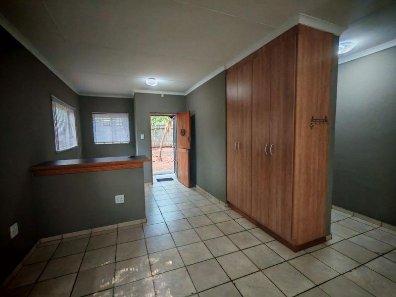 An open-plan living area featuring tiled flooring, built-in wooden cupboards, a breakfast counter, and direct access to the exterior.