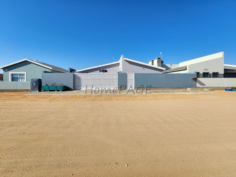 Front exterior view of the property featuring a gated entrance, boundary wall, and driveway access.