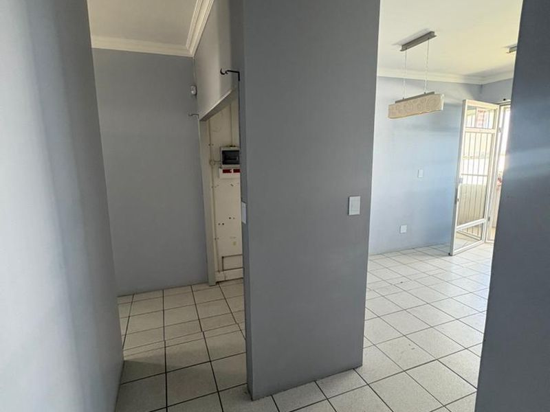 An open-plan office space featuring neutral grey walls, ceramic floor tiles, crown molding, and a central partition wall with an integrated electrical distribution board.