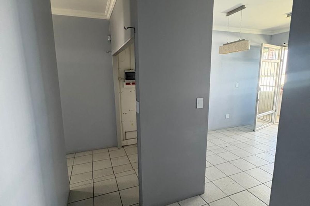 An open-plan office space featuring neutral grey walls, ceramic floor tiles, crown molding, and a central partition wall with an integrated electrical distribution board.