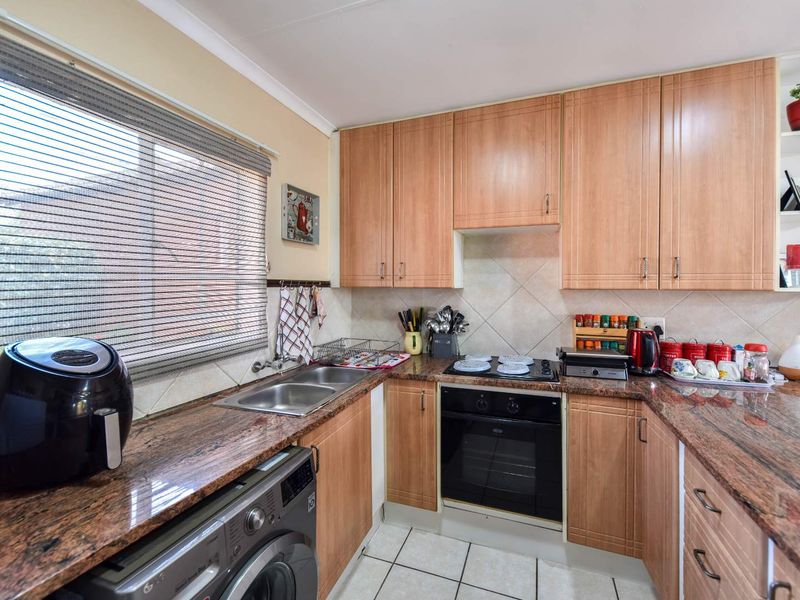 A functional kitchen featuring granite countertops, laminate cabinetry, a built-in oven with electric hob, and a double basin sink with tiled backsplash.