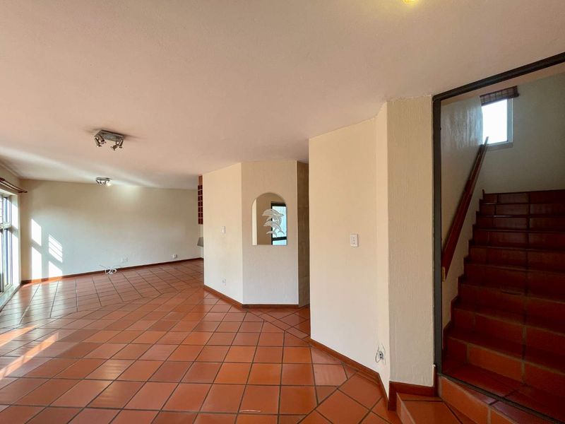 Spacious open-plan living area featuring traditional terracotta floor tiles, a built-in wall niche, and a staircase with a wooden handrail.