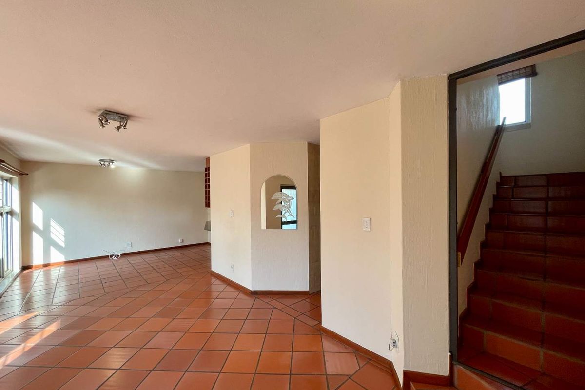 Spacious open-plan living area featuring traditional terracotta floor tiles, a built-in wall niche, and a staircase with a wooden handrail.