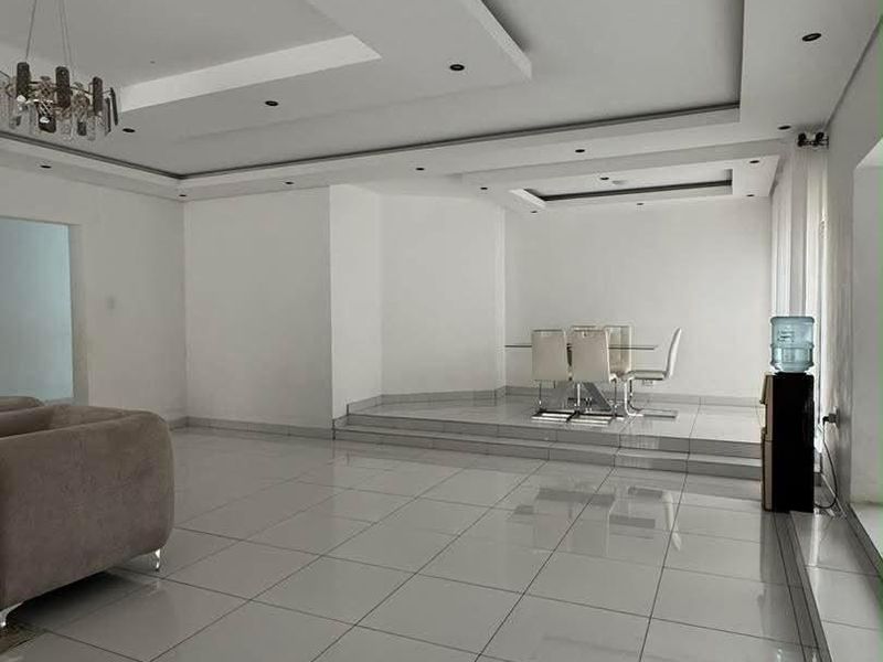 Spacious open-plan living and dining area featuring modern tiled flooring, a raised dining platform, and a sophisticated recessed ceiling with integrated downlighting.